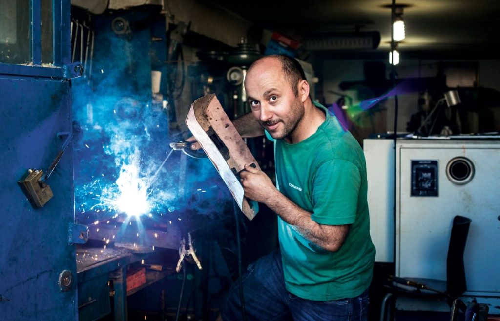 man wielding some metal while smiling at the camera showing the value of labour day