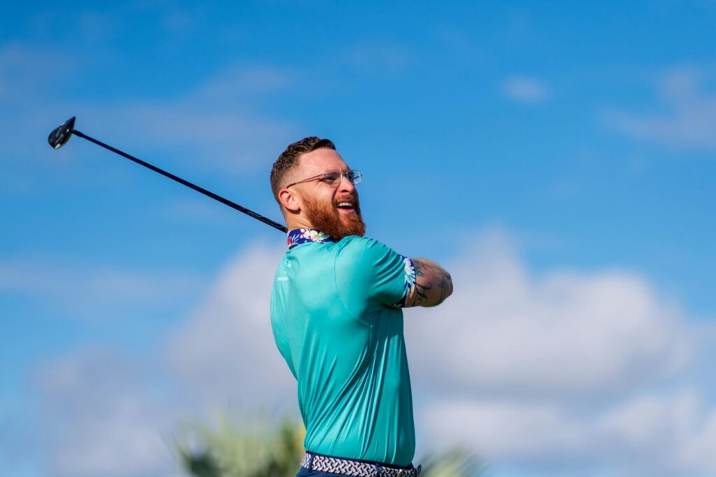 a man with sky blue tshirt striking a golf ball