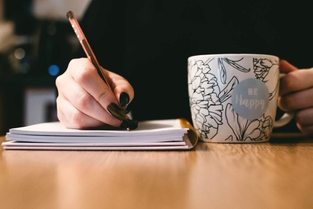 image of woman writing on a notebook with mug close to her practicing the tips on writing a limerick poem