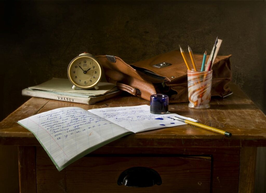 image of an alarm clock, pencil box, quill, ink, bag, book, and notebook on top of a drawer shows someone was writing about tips on writing a limerick poem