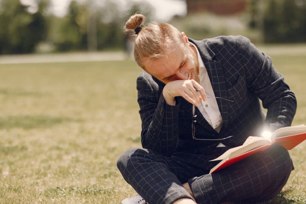 image of man reading a book and laughing while he’s sitting down on a grassy field analyzing the different tips on writing a limerick poem