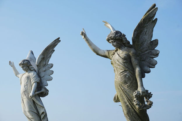 Two stone statues of angels, their hands pointing upward.