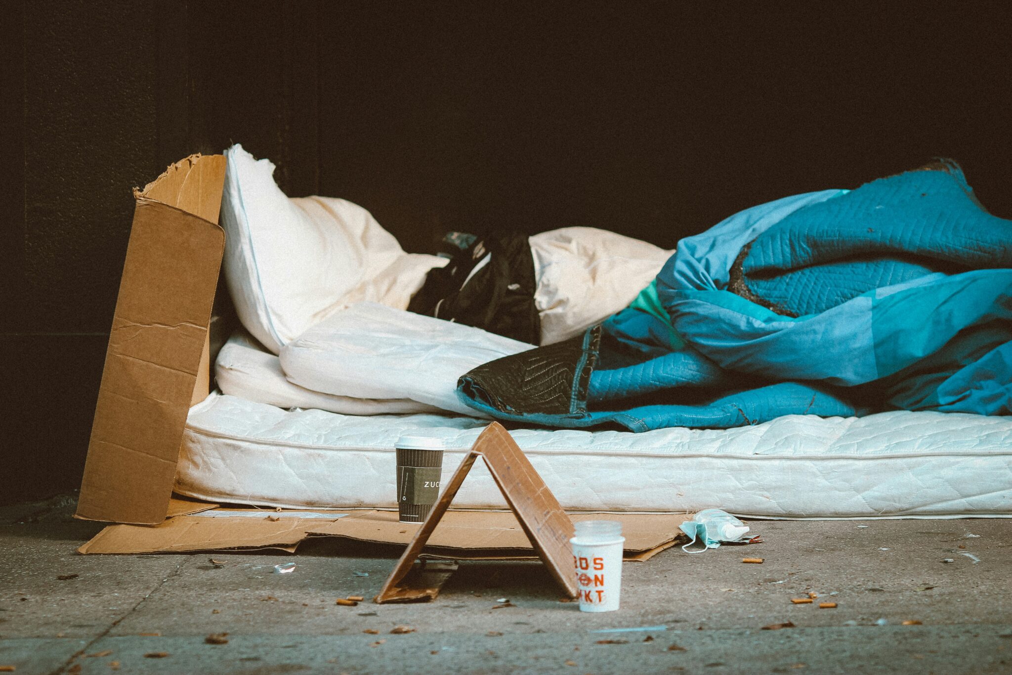 A mattress, pillow, and sheets on a cardboard lying on the street.