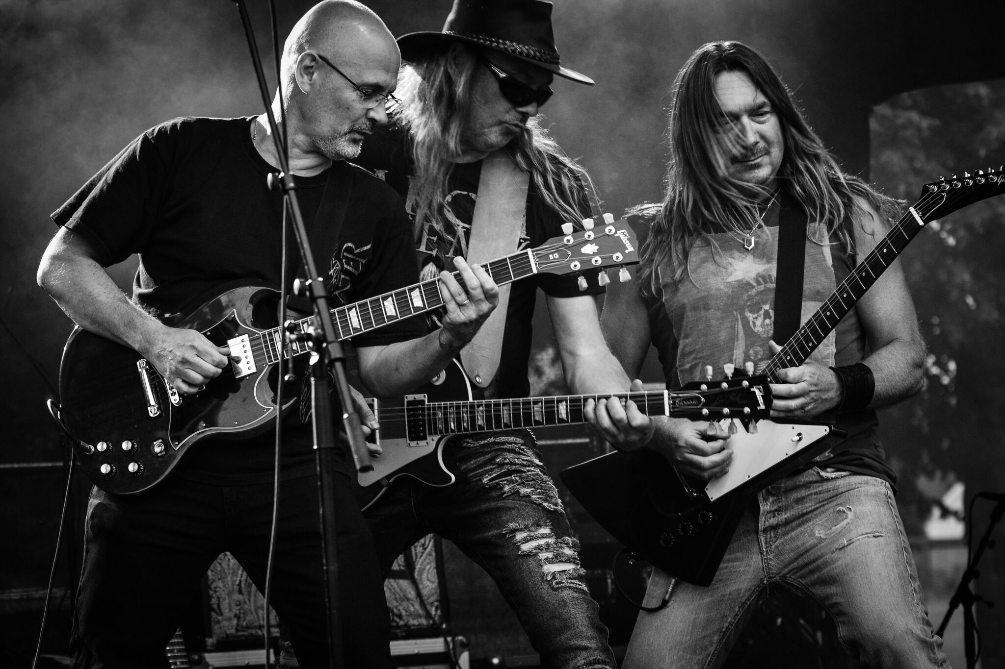 Three guitarists in black and white showing off their guitar solo skills in a live concert.