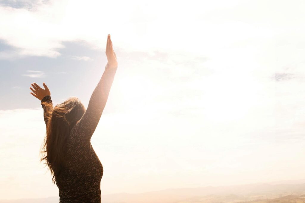 A woman with her arms spread under the sky.