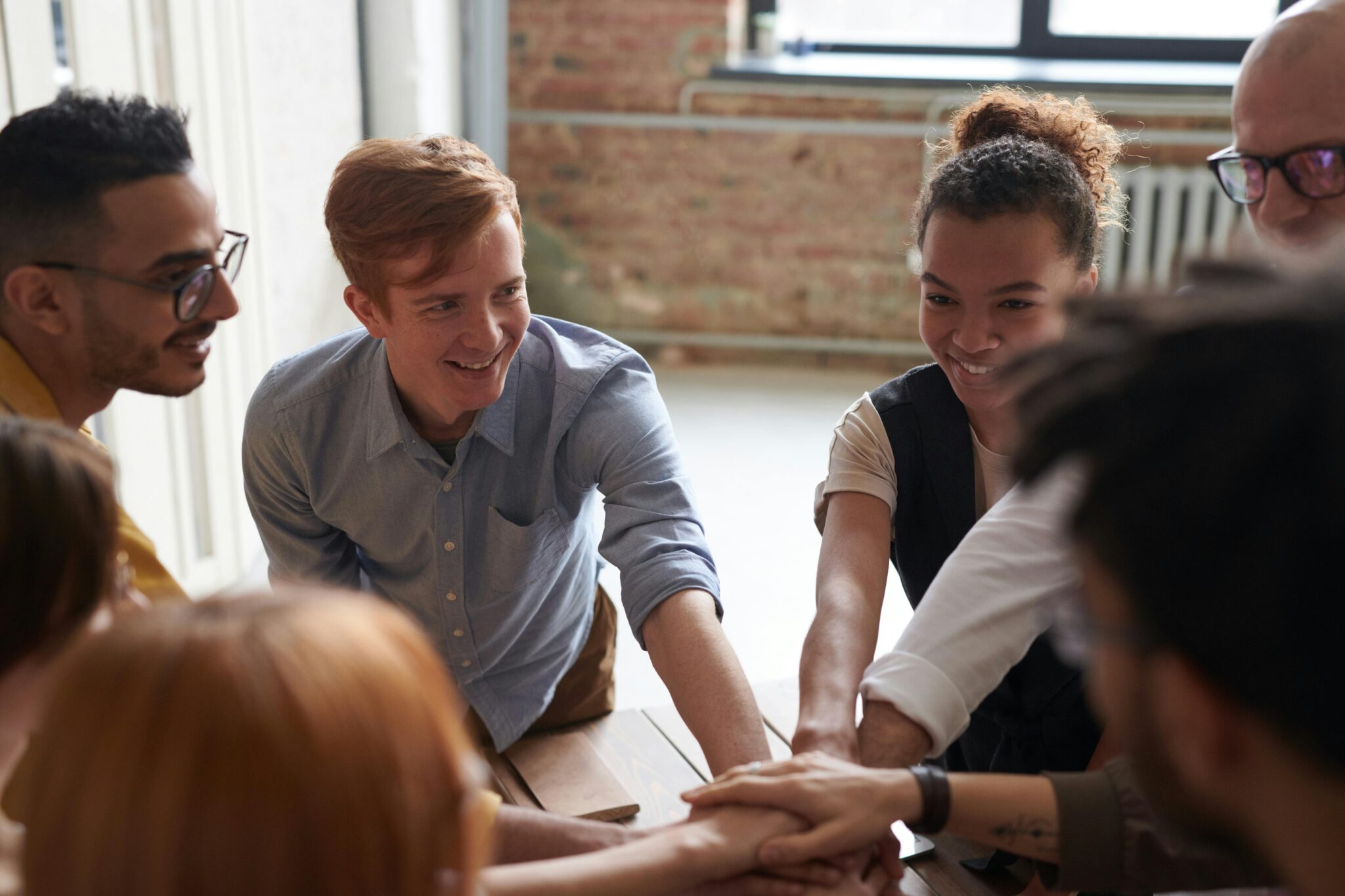 A group of young people happily putting their hands on top of each other’s’ hands, as a sign of motivation and creating safe spaces for the youth.