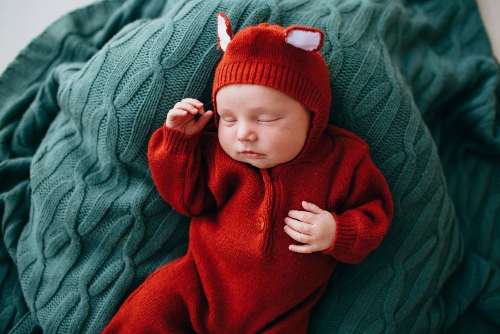 A baby in a red onesie with ears.