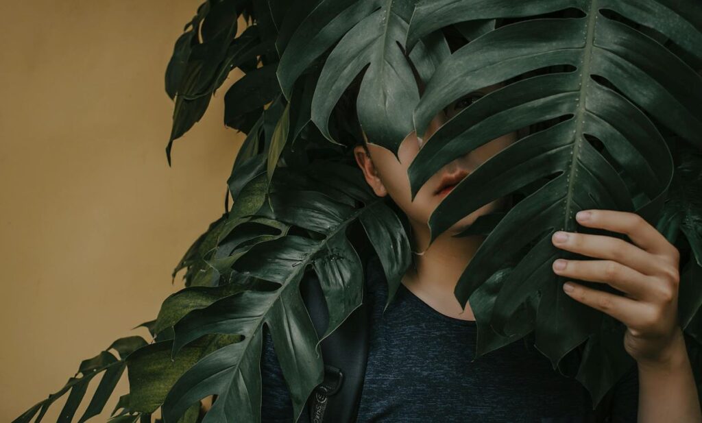 A man hiding his face behind leaves.