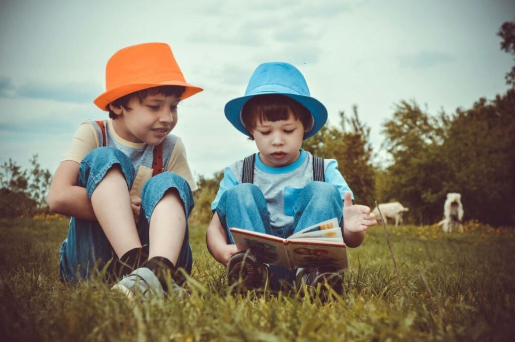 Two kids reading a book outside.