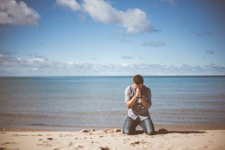 a person kneeling and praying along the shore, showing steadfastness in faith