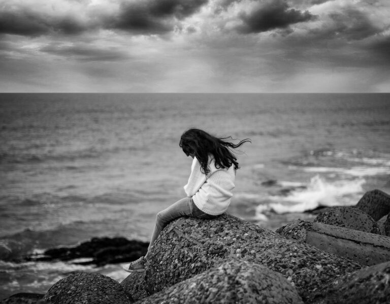 a photo of a woman sitting near the ocean reflecting finding god at rock bottom